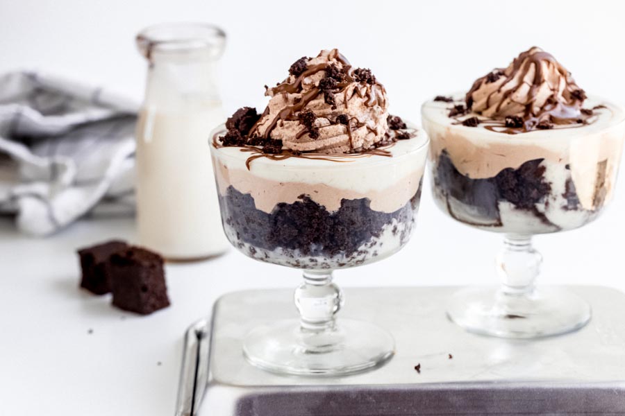 Two chocolate trifles side by side with layers of chocolate cake, chocolate whipped cream and vanilla pudding.