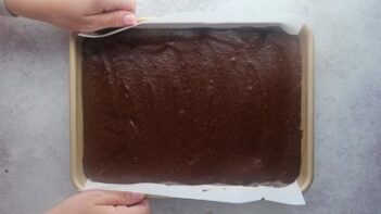 Hands holding a baking sheet filled with chocolate cake batter.