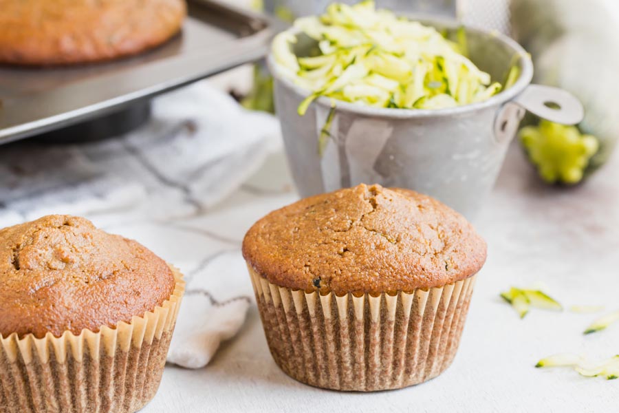 a fluffy muffin sits in front of grated zucchini in a measuring cup