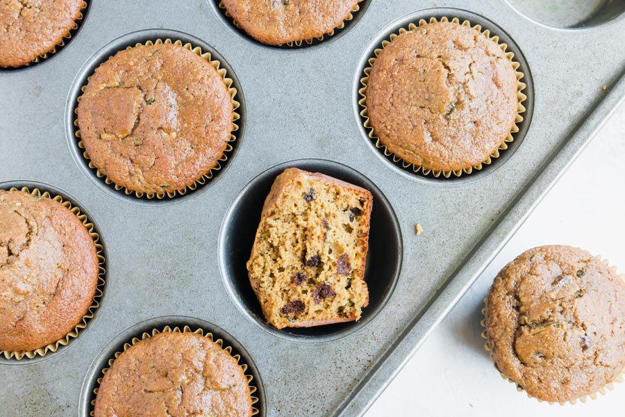 chocolate muffins in a tray with a half muffin facing up showing the chocolate chips