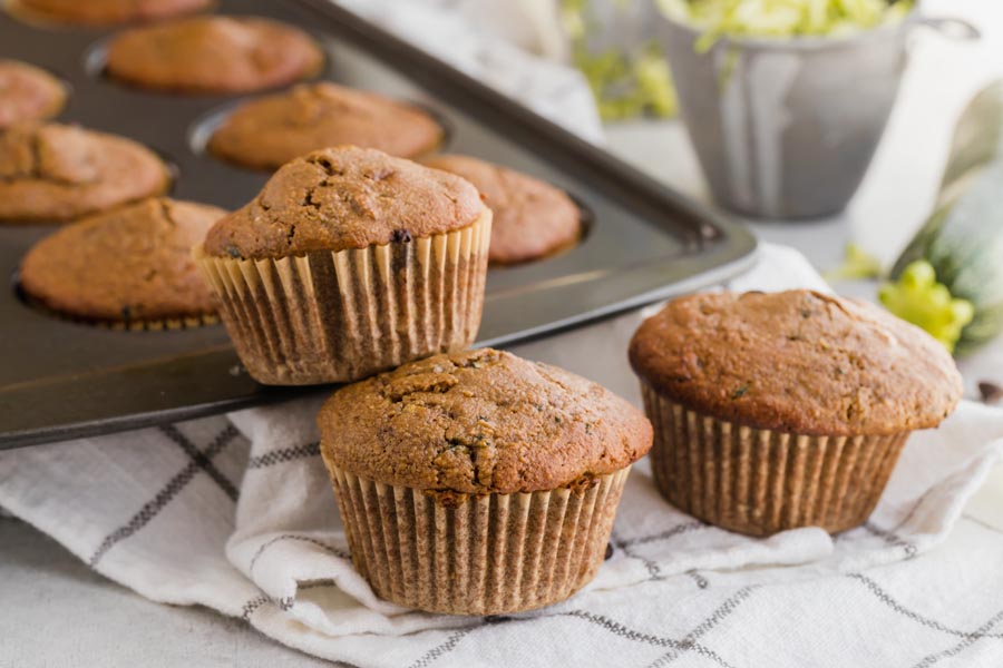 three zucchini muffins in front of a muffin pan