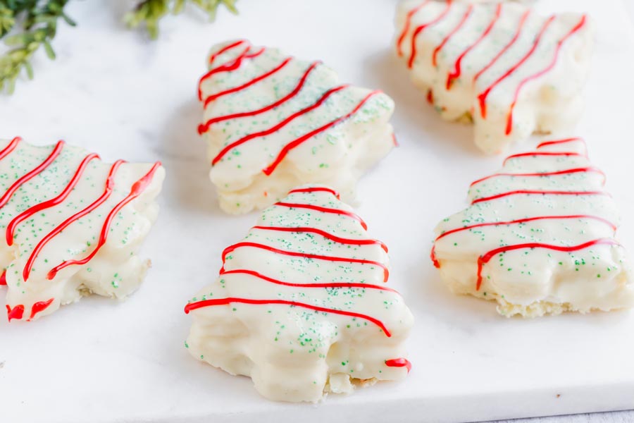 Five snack cakes on a marble slab in the shape of christmas trees and covered with white chocolate, green sprinkles and red stripes.