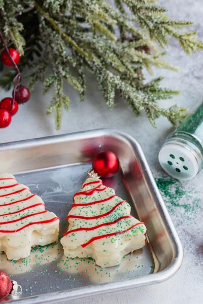 Two white cakes in the shape of trees on a baking sheet with green sprinkles scattered around.