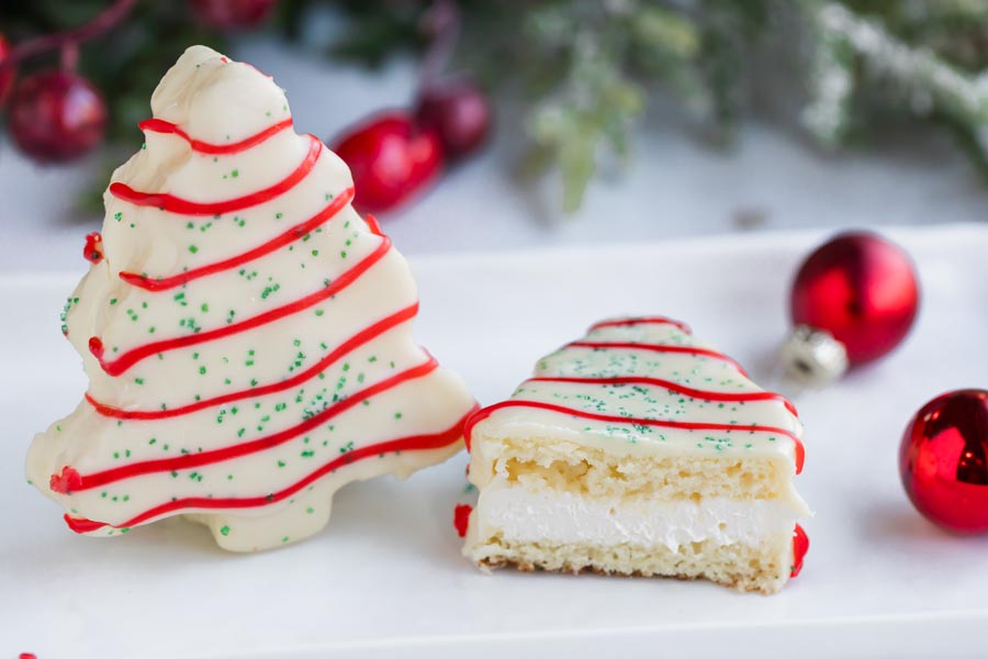 A white Christmas tree cake standing next to a white cake cut in half showing the layers of spongy white cake and creamy meringue buttercream frosting.