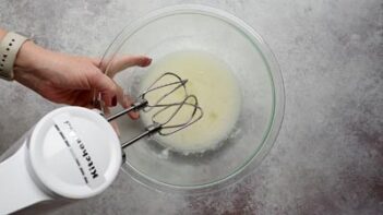 Mixing egg whites with sweetener in a glass bowl with an electric mixer.
