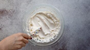 A hand uses a spatula to show the creamy Swiss meringue buttercream frosting.