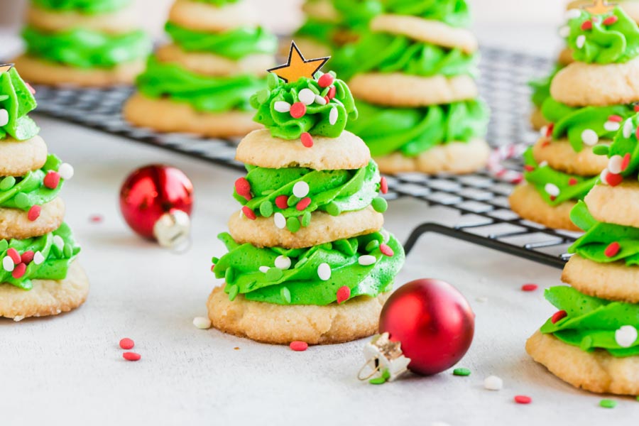 Three cookies separated by frosting decorated like a Christmas tree and topped with a star next to red bulbs.