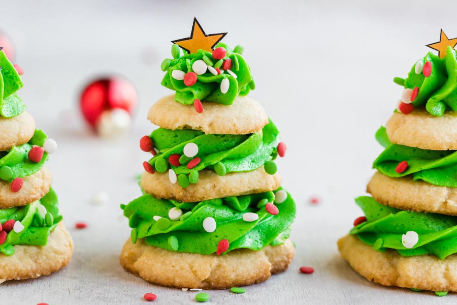 Three Christmas tree cookies decorated with red, white and green confetti sprinkles and gold stars on top.