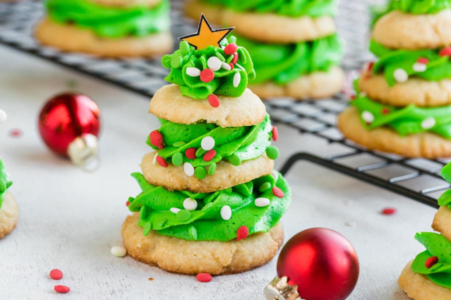 Close up of a three tiered Christmas cookie separated by green frosting and sprinkles all over.