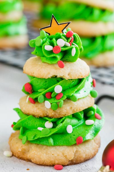 Sugar cookies sandwiched with green frosting in a way to resemble a tree and topped with a gold star.