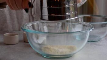 Holding a sifter and sifting almond flour into a bowl.