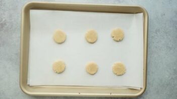 Six small round cookies on a baking tray lined with parchment paper.