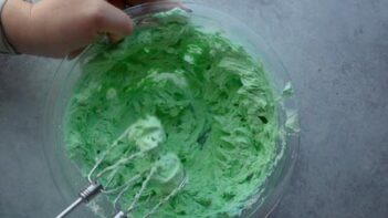 An electric mixer mixing green frosting in a bowl.