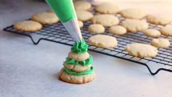 Piping green frosting on top of a tiered stack of cookies.