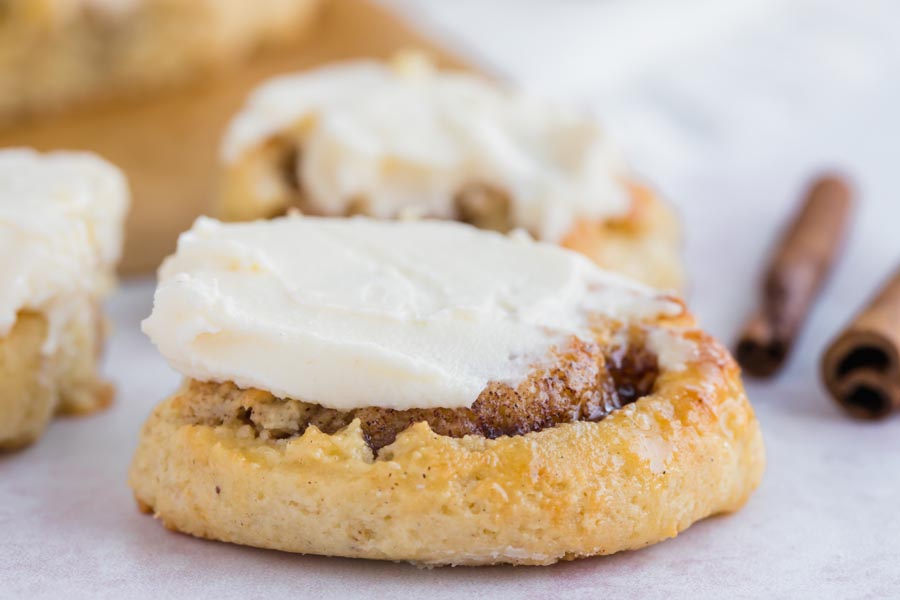 keto cinnamon roll topped with cream cheese frosting next to cinnamon sticks