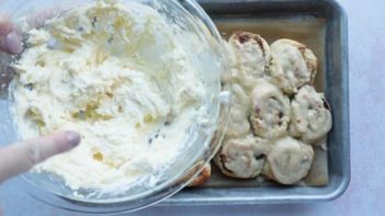 cream cheese frosting in a bowl over a tray of cinnamon buns
