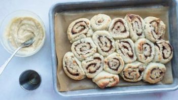 buttery sweet glaze mixed in a bowl next to a tray of cinnamon rolls