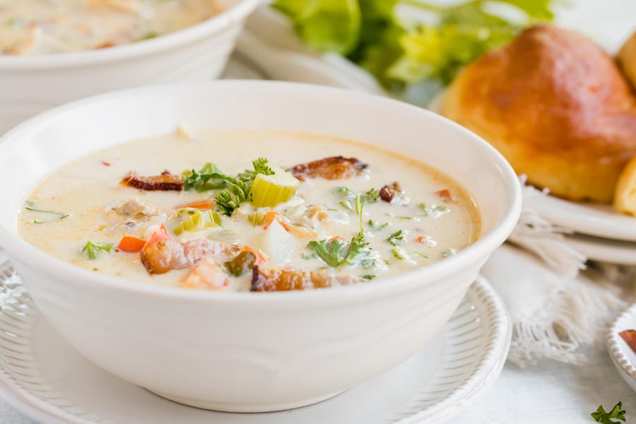 a bowl of clam chowder with keto rolls behind
