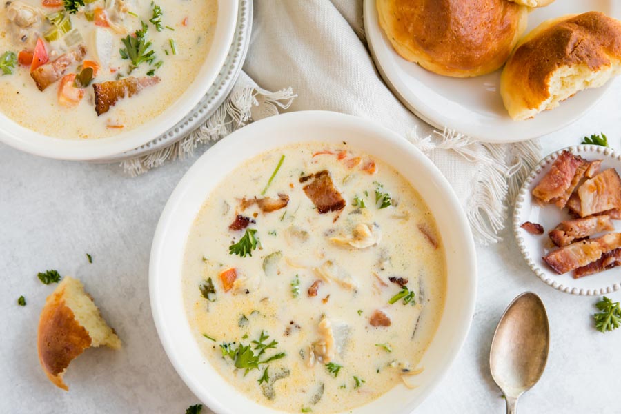two bowls of creamy soup on the dinner table with rolls and bacon