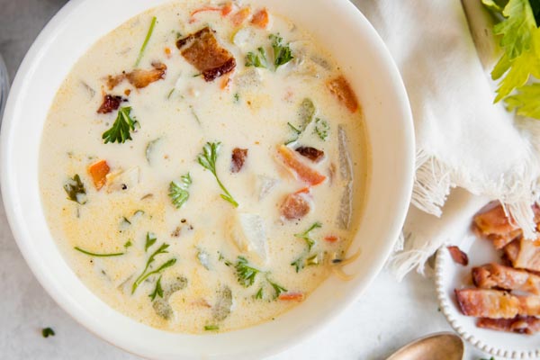 a hearty bowl of clam chowder next to cooked bacon and celery