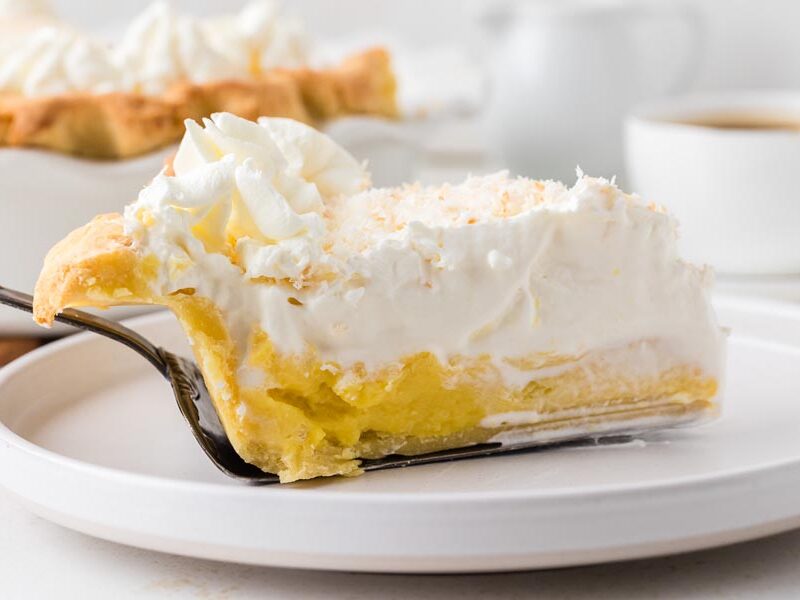 A slice of coconut cream pie placed on a white plate with a pie spatula.