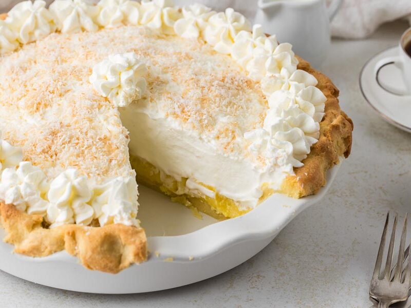 A slice taken out of a coconut cream pie topped with whipped cream and toasted coconut.