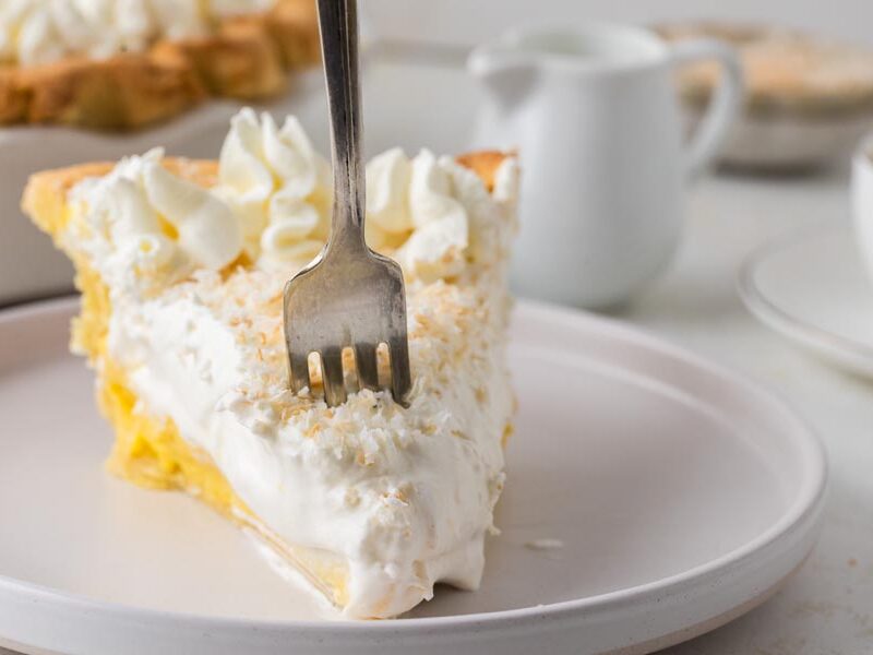 A fork digging into a slice of coconut cream pie on a plate.
