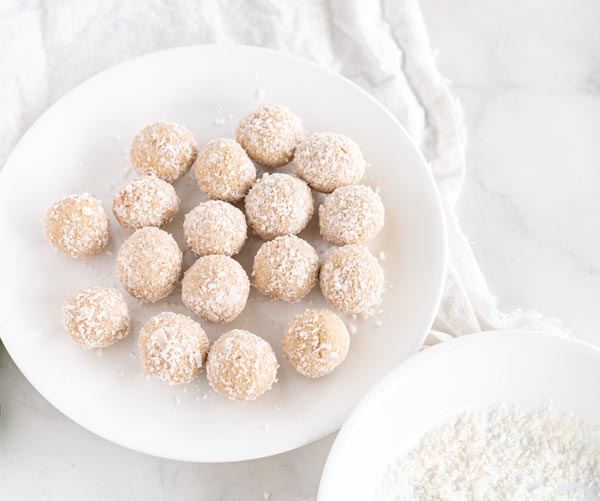 coconut covered balls on a plate with shredded coconut flakes in a bowl