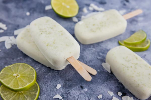 a group of frozen popsicles the counter with lime slices and coconut chips near them 