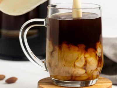 Homemade keto coffee creamer being poured into a mug of hot black coffee, creating creamy swirls.