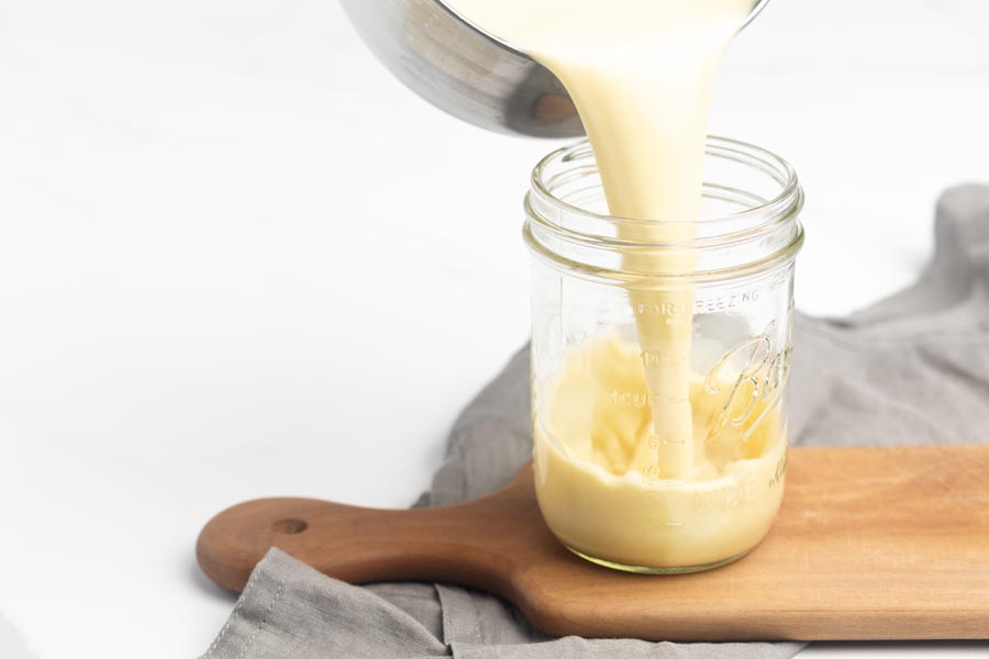 Thick and creamy homemade keto coffee creamer being poured into a glass mason jar for storage.