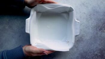 Hands holding a white square baking dish lined with parchment paper.