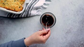 A hand holding a spoon of melted chocolate over a bowl.