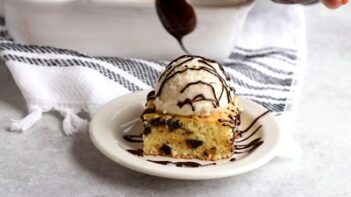 Drizzling melted chocolate sauce over ice cream sitting on top of a cookie bar.