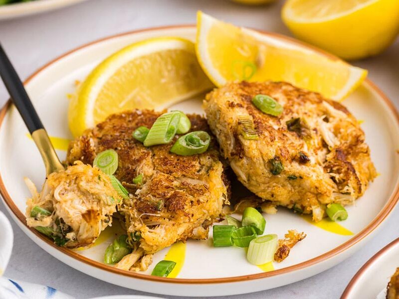 Two crab cakes on a plate with lemon slices.