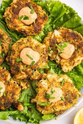 Six keto crab cakes on a bed of lettuce topped with sauce and chives.