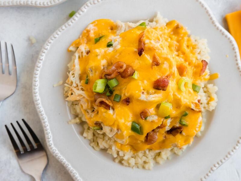 a plate with melted cheddar cheese on top of shredded chicken and cauliflower rice next to two forks
