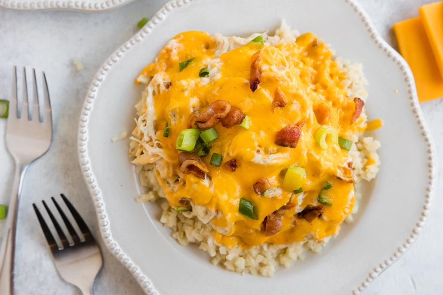 a plate with melted cheddar cheese on top of shredded chicken and cauliflower rice next to two forks