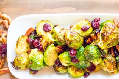 a platter of roasted brussels sprouts topped with pecans and cranberries