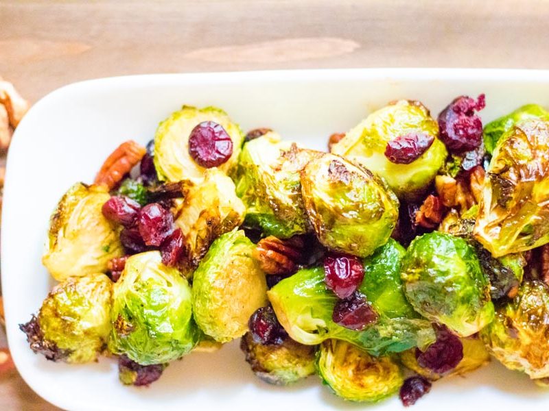 a platter of roasted brussels sprouts topped with pecans and cranberries