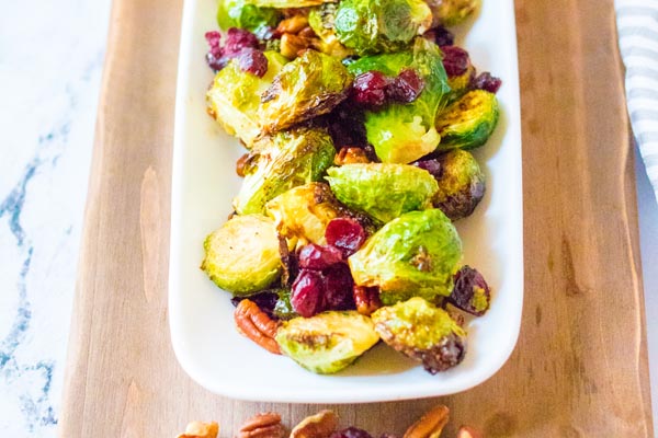 a plate of cranberry and pecan brussels sprouts on a wooden board