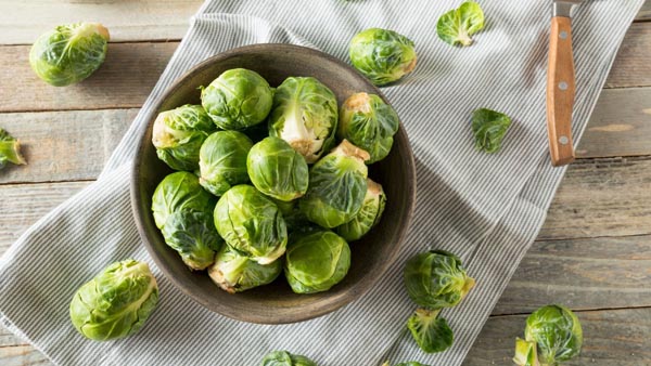 a bowl of whole brussels sprouts that need to be trimmed with a knife