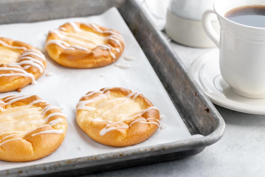 a baking sheet with four danishes next to a cup of coffee