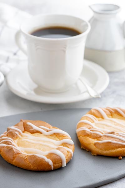 two danishes filled with cream cheese on topped with ice in front of a cup of coffee and cream