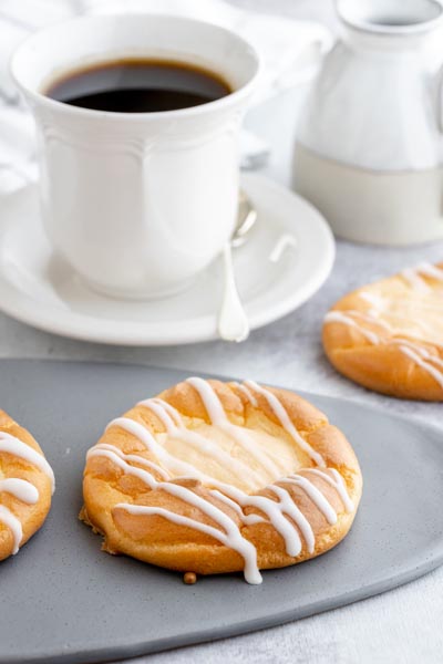 a gray plate with a danish filled with cream cheese in front of a cup of black coffee