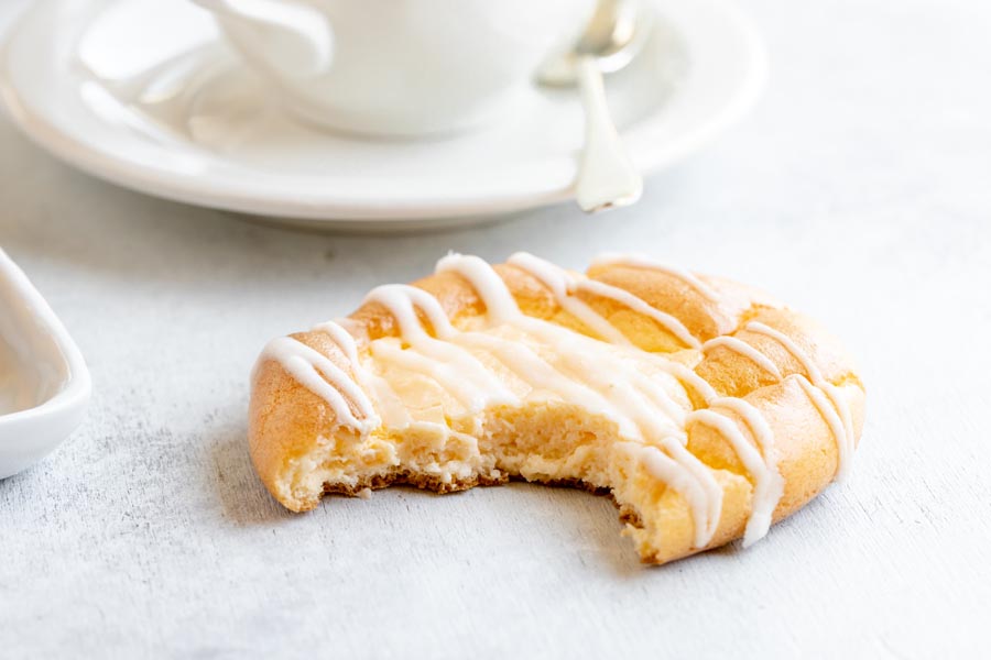 a bite taken out of a cream cheese danish in front of a white coffee mug