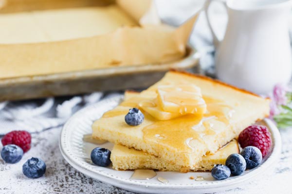 square pancakes from a sheet pan topped with butter, syrup and berries
