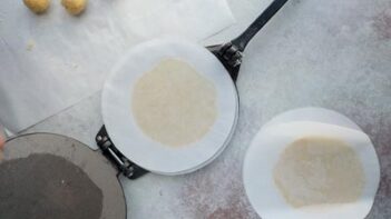 a flat tortilla in between parchment circles on a tortilla press