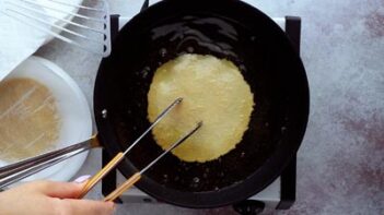 using tongs to press down a tostada shell in oil to fry