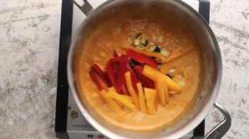 a saucepan with bell pepper in a curry sauce